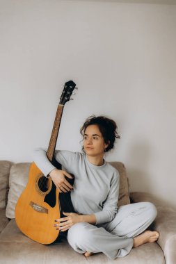 Evdeki kanepede otururken gitar çalan güzel bir genç kadın.