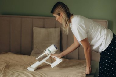 Yatak odasındaki döşekleri süpürmek için elektrikli süpürge kullanan kadın.