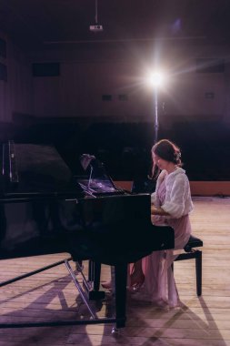 Sahne, konser ve performans, eğlence ve yetenek gösterisi için piyanosu olan bir kadının arkası. Müzisyen, piyanist ve kişi tiyatro için enstrüman, müzik ve senfoni çalıyor.