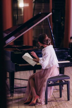Genç bir kadın evde piyano çalışıyor ve nota okuyor.