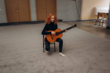 Genç kızıl saçlı kadın yatakta ukulele oynuyor.