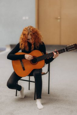 Genç kızıl saçlı kadın yatakta ukulele oynuyor.