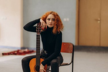 Güzel kızıl saçlı kadın dışarıda gitar çalıyor.