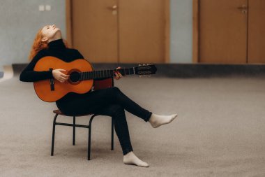 Genç kızıl saçlı kadın yatakta ukulele oynuyor.