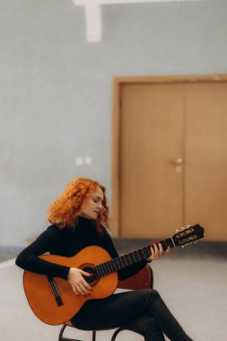 Evinde gitar çalan rahat bir kızıl kadın.