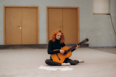 Kızıl saçlı bir kadın gitar çalışıyor.