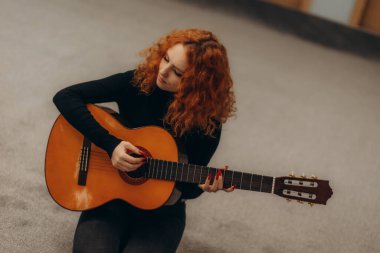 Mutlu genç bir kadın, hafta sonları evdeki rahat oturma odasında oturup dinlenirken gitar çalıyor..