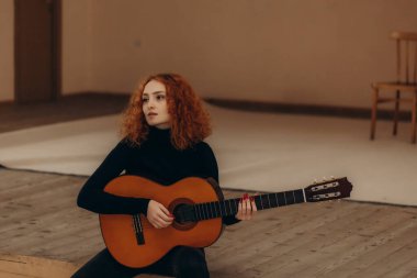 Kızıl saçlı bir kadın sahnede oturur ve gitar çalar.