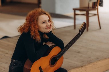 Rüya gibi kızıl saçlı bir kız sahnede gitar ile oturuyor.