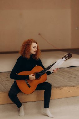Kızıl saçlı bir kadın sahnede oturur ve gitar çalar.