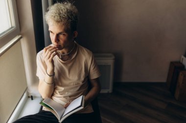 Sarışın bir adam, sarışın bir adam pencerenin kenarında kitap okuyor. Pencereden hayallere dalmış, pencerenin kenarında bir kitap görüyor.