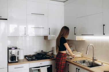 Yemek pişirirken modern bir mutfağın yanında duran güzel vücutlu genç bir kadın. Arka plan