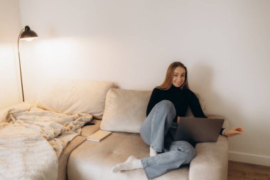 Concentrated millennial girl sit on couch working on laptop browsing internet at home during lazy weekend, focused young woman freelancer busy using computer surfing wireless web shopping online clipart