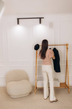 Neşeli genç bir kadın raftan kıyafet seçiyor, alışverişi seviyor.