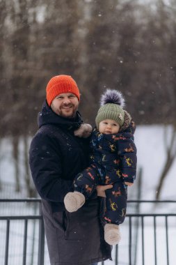 Kışın parkta yürürken babasının kollarında bir çocuğun portresi.