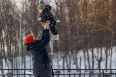 Baba, buz gibi bir günde dışarıda eğlenirken oğlunu kaldırıyor, mutlu baba ve çocuk kış parkında oynuyor, karlı havanın tadını çıkarıyor, yeni yılı açık havada geçiriyor.