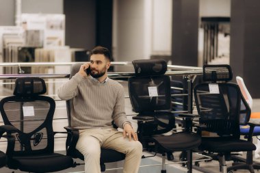 Bilgisayar sandalyesindeki bir adam ofisi için rahat bir sandalye seçer.