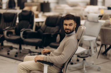 Adamın biri mobilya mağazasında bilgisayar sandalyesini deniyor. 