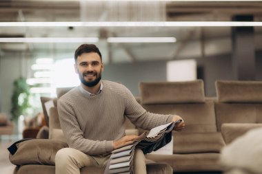 Bir adam kanepe renkleri ve kumaşlardan oluşan bir katalog tutuyor. Kanepe almak ve seçmek.