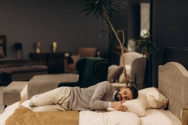 Bir adam mobilya mağazasında bir yatakta test yapıyor ve yalan söylüyor.