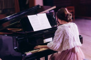 Zarif bir ortamda zarif bir şekilde piyano çalan bir kadını tasvir eden huzurlu bir an. Kıyafeti ve atmosferi entellektüellik, yaratıcılık ve ahenk duygusu taşıyor..