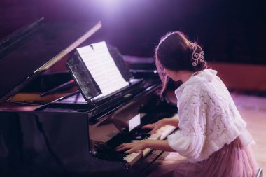 Bir kadın zarif bir şekilde sıcak bir ortamda piyano çalar, zarafeti ve müzik tutkusunu vurgular, tarzında ve duruşunda belli eder..