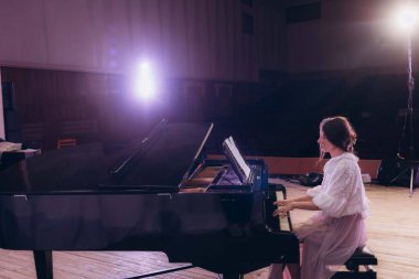 A female pianist in a stylish outfit playing a grand piano on a dimly lit stage, evoking a serene and artistic ambiance, spotlighted against the dramatic atmosphere of an empty concert hall. clipart