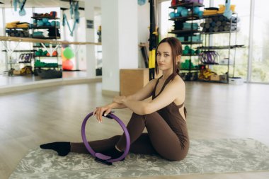 Kendine güvenen bir kadın, parlak, temiz bir spor salonunda pilates yüzüğüyle egzersiz yapıyor. Kullanılabilir çalışma ekipmanları ile güç, denge ve farkındalık egzersizleri için ideal fitness ayarları.