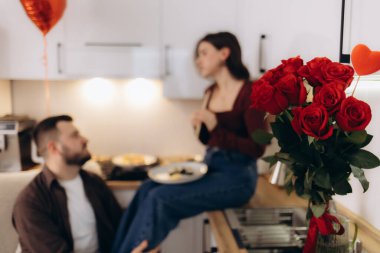 Mutfakta kırmızı güllerle kalp şeklinde bir balonun olduğu bir çift arasında romantik bir an. Yumuşak ışıklandırma sıcak bir atmosfer yaratıyor. Kutlamalar, şefkat ve aşkı ifade etmek için mükemmel..