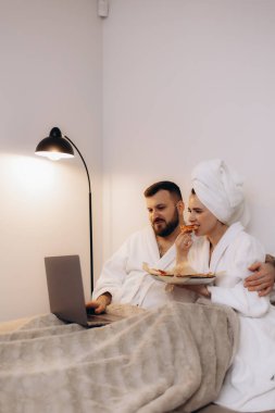 Sıcak, modern bir ortamda birlikte yemek yiyen bornozlu bir çiftin samimi bir sahnesi..