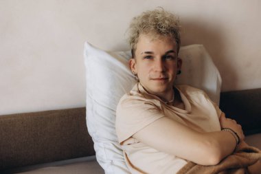 Yatağa yaslanmış, sükunet ve güven saçan, doğal ışıklandırmayla huzurlu atmosferi geliştiren bir insan..