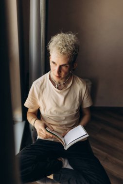 Genç bir adam pencerenin kenarında oturur, sakin bir ışıkla çevrili bir kitabı tutar ve okur..