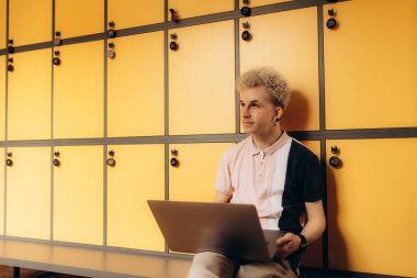 Sarı dolapların yanında oturan şık bir şahıs dizüstü bilgisayarla çalışıyor. Çevre odaklanmayı, modern estetiği ve çalışma ve rahatlamaya uygun rahat bir atmosferi tasvir eder..