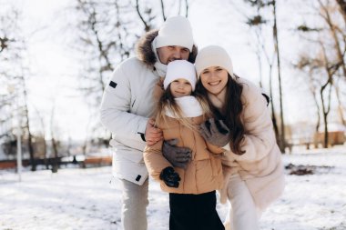 Sıcak giyimli mutlu bir aile, güzel bir kar parkında dışarıda kaliteli zaman geçiriyorlar. Bu görüntü bir kış günü neşe ve beraberliği yakalar..