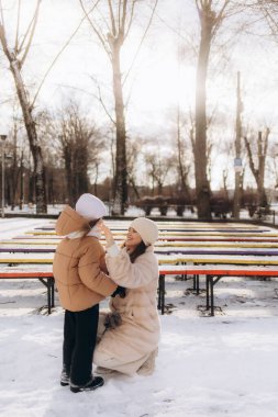 Neşeli bir anne ve çocuk, dışarıda, karlı bir parkta vakit geçirirken kaynaşıyor..