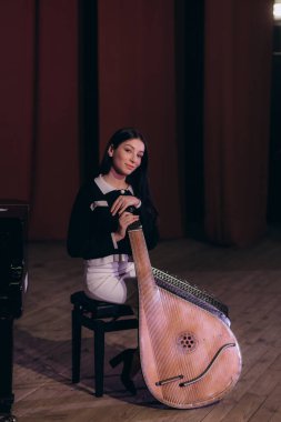 Genç bir kadın, sanat ve kültürü vurgulayarak geleneksel bir bandura ile sahnede müzik yapıyor..