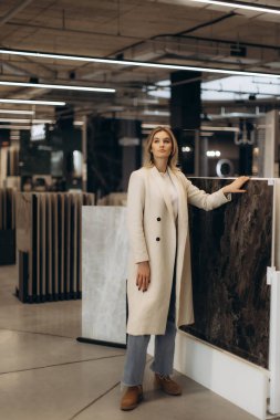 Elegant woman in a modern industrial-style showroom examining premium-quality interior decoration panels and surfaces. She exhibits a sophisticated style amidst contemporary architectural elements, highlighting interior design trends. clipart