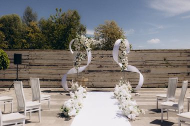 Beyaz çiçek aranjmanları, dekoratif sandalyeler ve manzaralı manzaralı bir düğün töreni. Parlak, güneşli bir gökyüzü altında zarif ve çekici bir kutlama için mükemmel..
