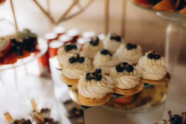 Krem şanti ve taze yaban mersinli hamur işleri içeren bir tatlı büfesinin yakın çekimi. Düzenleme sofistike ve nefis bir atmosfer yaratıyor..