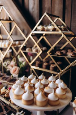 Limonlu pasta, pasta ve pastaların yer aldığı güzel bir tatlı düzenlemesi dekoratif altın raflar ve çiçeklerle romantik bir düğün zeminine karşı kurulmuş, sıcak ve şenlikli bir ortam yaratıyor..