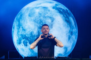 Muhteşem bir dolunay projeksiyonunun önünde duran bir DJ, bir müzik etkinliğinde ilgi çekici bir ortam oluşturur, heyecan verici ve canlı bir atmosferi teşvik eder..