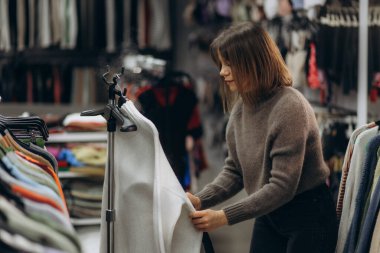 Bir kadın aydınlık bir butik dükkanında giysi eşyaları ayarlıyor, moda trendleri sergiliyor..