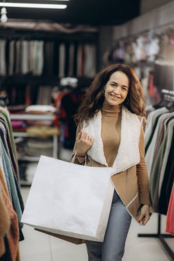 Perakende giyim mağazasından alışveriş yapan neşeli bir kadın, elinde büyük bir kese kağıdıyla. Sahnede eğlence, moda ve perakende terapisi vurgulanıyor. İlgi çekici bir ticari deneyimin özünü yakalıyorlar..