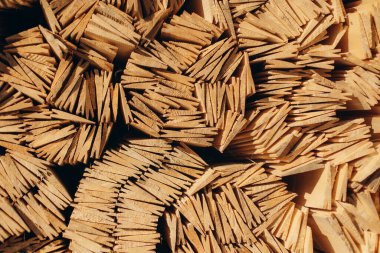 Düzenlenmiş tahta kıymıklarının güneş ışığıyla aydınlatılmış desenli desenleri vurgulayan detaylı görüntüsü. Altın ahşap parçalar, tasarım ve kavramsal amaçlar için ideal soyut ve doğal bir sanatsal kompozisyon oluşturur..