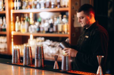 Canlı bir barda barmenlik yapan profesyonel bir barmen. Etrafı barmenlik ekipmanlarıyla çevrili ve gece hayatı sahnesi yaratıyor..