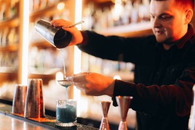 Becerikli bir barmen özel bir içecek koyar süzgeç ve titretici kullanarak, sıcak ışıklandırılmış, sosyal bar atmosferinde miksoloji uzmanlığı sergiler.