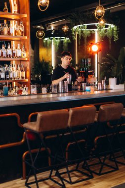 Bartender working at a modern bar with stylish decor, preparing cocktails amidst a warm, inviting ambiance. clipart