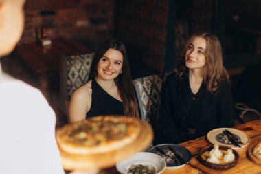 İki arkadaş sıcak ve davetkar bir atmosferde sıcak bir restoranda birlikte yemek yiyip gülümseyerek ve harika yemekler yiyerek eğleniyorlar..