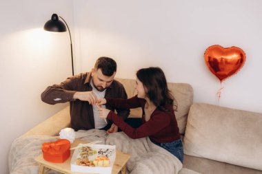 Bir çift sıcak bir akşamın tadını çıkarır, suşiyi paylaşır, sevgiyi vurgulayan süslemelerle. Sıcak gülümsemeleri ve hassas etkileşimleri modern ve güzel dekore edilmiş bir yerde romantik ve samimi bir atmosferi yansıtıyor..