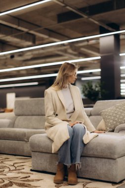 Modern mobilyaları olan şık bir iç mekânda rahat bir koltukta oturan zarif bir kadın rahat ve şık bir atmosfer sergiliyor, ev yaşamı veya moda ilhamı için mükemmel..